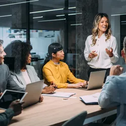 Female leader standing in conference room, advocating for the lab's priorities in front of seated executive colleagues