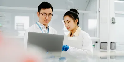 Two Asian scientists working on computer and asking questions about their research
