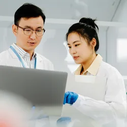 Two Asian scientists working on computer and asking questions about their research