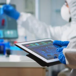 Back view of scientist in coverall analyzing virus evolution looking on digital tablet.