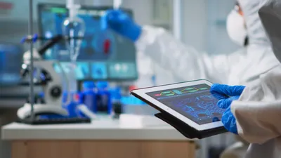 Back view of scientist in coverall analyzing virus evolution looking on digital tablet.