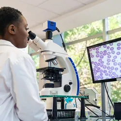 Lab technician using a microscope and analyzing digital slide images