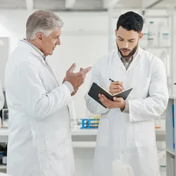 Two scientists in white coats converse about lab safety and risk perception.