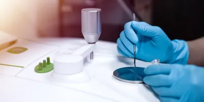 Image shows gloved hand from scientist using a Fourier Transform Infrared spectrometer (FTIR) to analyze drugs in identifying chemical identity.