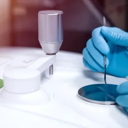Image shows gloved hand from scientist using a Fourier Transform Infrared spectrometer (FTIR) to analyze drugs in identifying chemical identity.