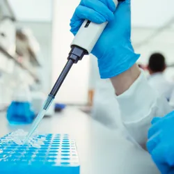 Scientist pipetting samples into tray in laboratory
