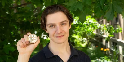 Researcher holds a sample of 3D-printable metal alloy in a garden.