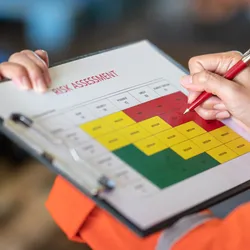 Action of a person is using ballpoint pen to marking on the risk assessment matrix table at "High risk" level.