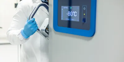 Scientist in a lab coat and gloves opening an ultra-low temperature freezer in a scientific laboratory