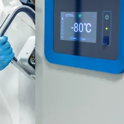 Scientist in a lab coat and gloves opening an ultra-low temperature freezer in a scientific laboratory