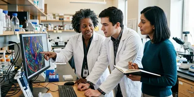 Three laboratory colleagues with different specialisms discuss results together at a workstation, illustrating the mixed skills a spatial biology team requires