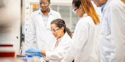 Female lab leader demonstrating safety training to three new hires during onboarding session.