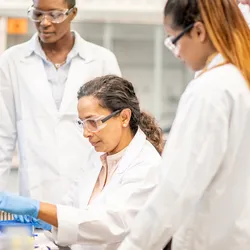 Female lab leader demonstrating safety training to three new hires during onboarding session.
