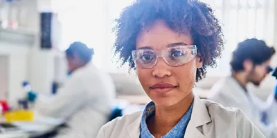 Portrait of a confident young female scientist sitting a table in a lab with colleagues working in the background