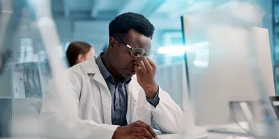 Man in lab coat experiencing digital eye strain while using a computer