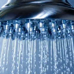 Close-up of a showerhead spraying water, relevant to decontamination practices.
