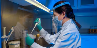 A female scientist in full PPE pipettes a solution into a container