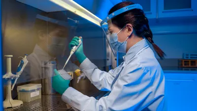 A female scientist in full PPE pipettes a solution into a container