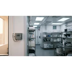 A GMP pharmaceutical cleanroom with wall-mounted IoT environmental monitoring sensors and a technician reviewing a cloud-based compliance dashboard on a tablet.