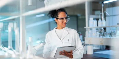 Portrait of a young Hispanic female chemist writing down the results on a clipboard.
