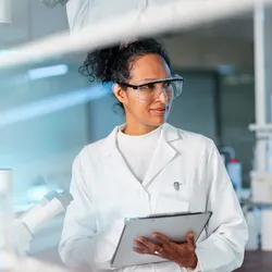 Portrait of a young Hispanic female chemist writing down the results on a clipboard.