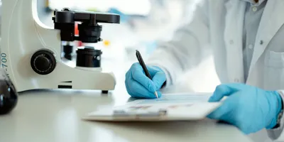 Laboratory professional writing notes next to a microscope during accreditation process