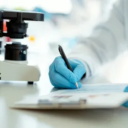 Laboratory professional writing notes next to a microscope during accreditation process