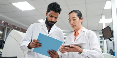 Low angle view of two lab professionals looking at tablet and clipboard during lab audit