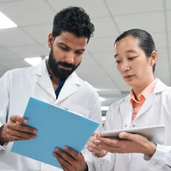 Low angle view of two lab professionals looking at tablet and clipboard during lab audit