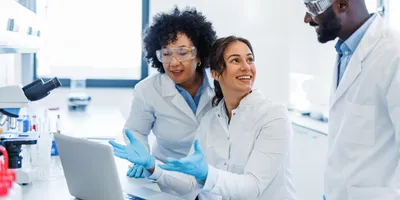 Three researchers engaged in a discussion near a laptop