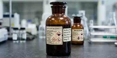 An amber reagent bottle with its supplier label intact and a smaller handwritten label added alongside rather than over it