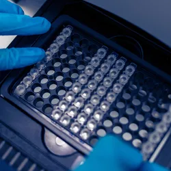 scientist putting test 96 well plate into real-time PCR machine