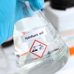 Person holding a flask labeled hydrofluoric acid with hazard symbol