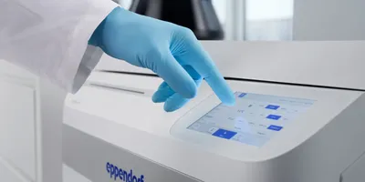 A gloved hand touches the 7-inch display of the Eppendorf SpinPro 8 R high capacity centrifuge, with a dark centrifuge rotor visible in the background.