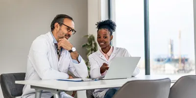 lab manager and lab operations manager sitting at table discussing results on laptop
